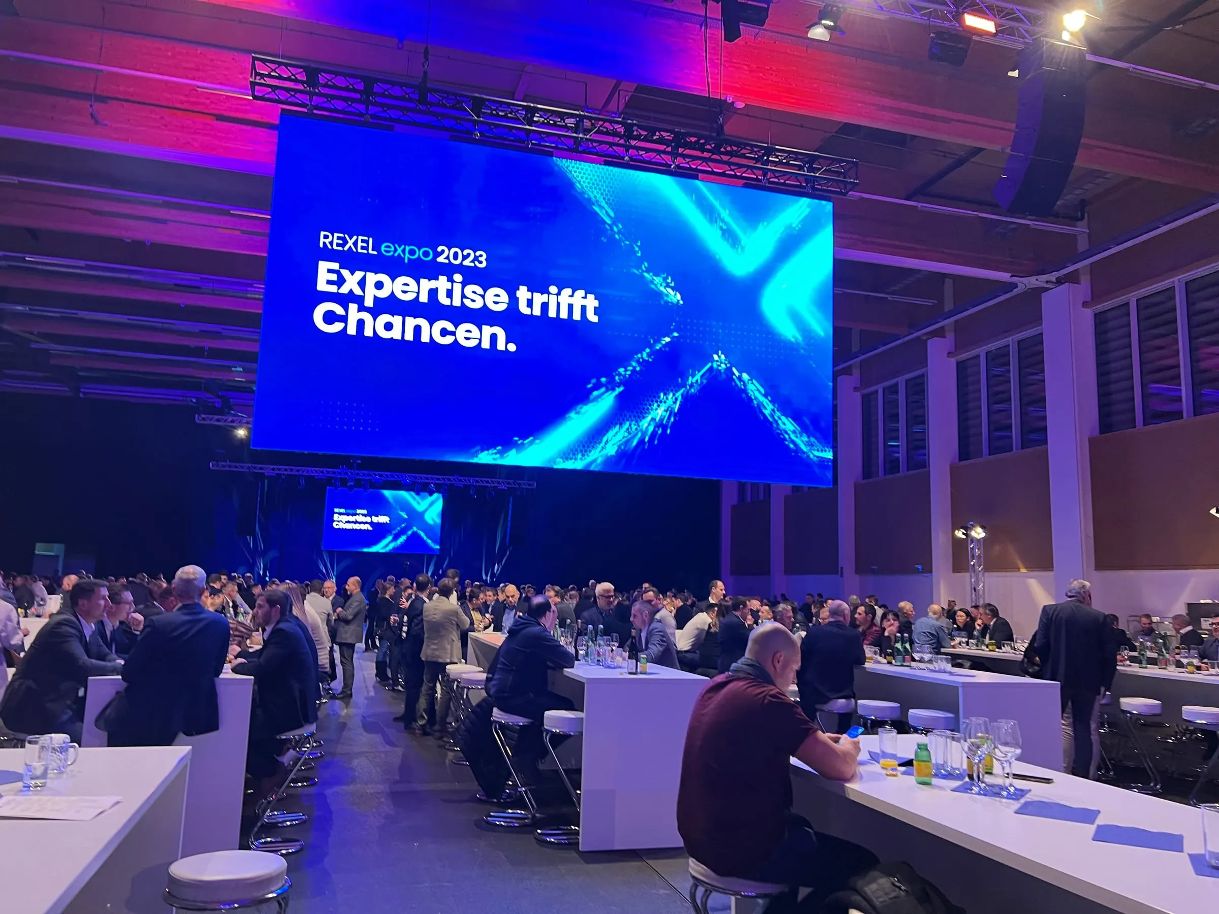 Große Messehalle mit Bühne, LED-Wand und Publikum bei einer Fachkonferenz