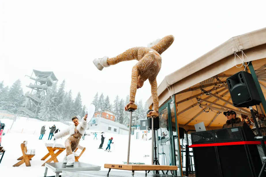 Akrobatin im Handstand auf einer Bühne vor der verschneiten Piste am Semmering