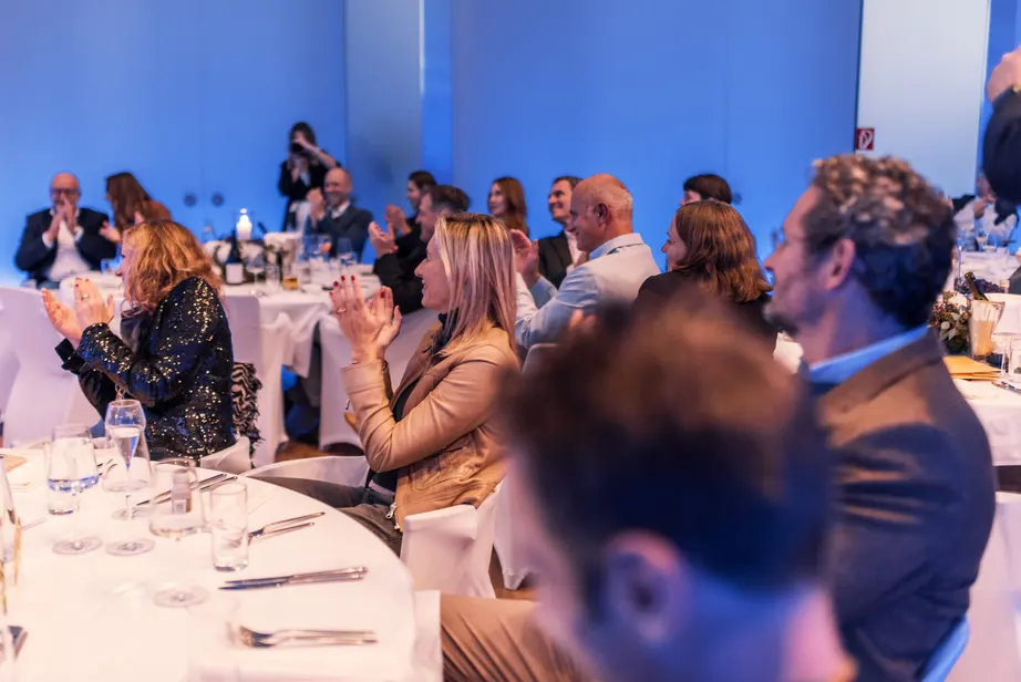Gäste an festlich gedeckten Tischen in einem hellen Saal mit blauem Licht